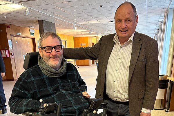 Cornwall Liberal Democrat councillor Jim Candy stands with his arm around a man in a wheelchair.