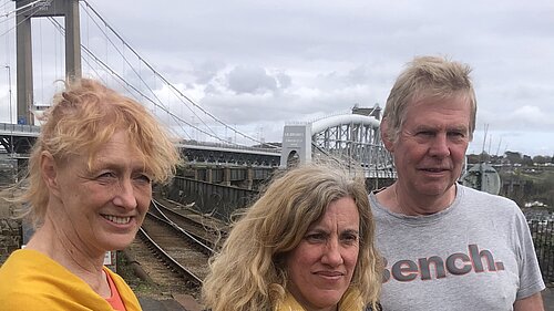 Three people, two women and one man, in the foreground, with the Tamar Crossing at Saltash in the background