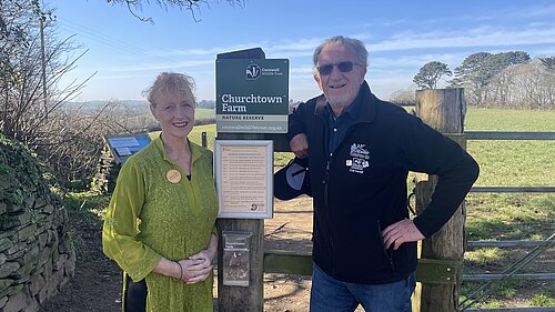 Cornwall Councillor Hilary Frank with Bob Austin, standing by a sign that says Churchtown Farm